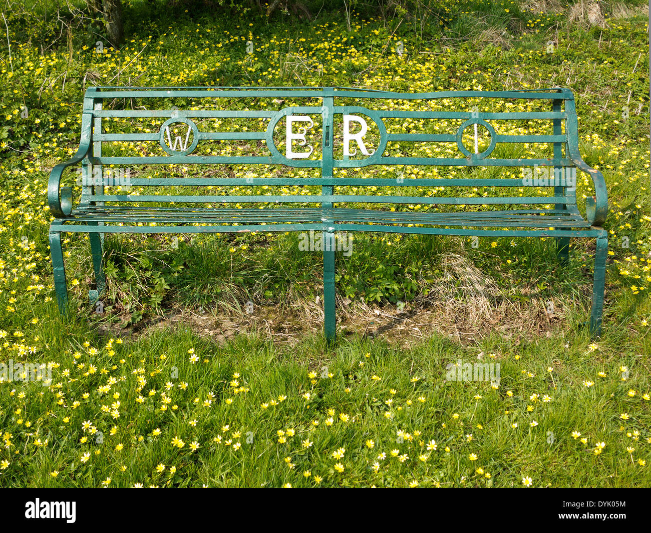 Green wrought iron bench with Women's Institute and Elizabeth Regina reference. On grassy background with lesser celandine Stock Photo