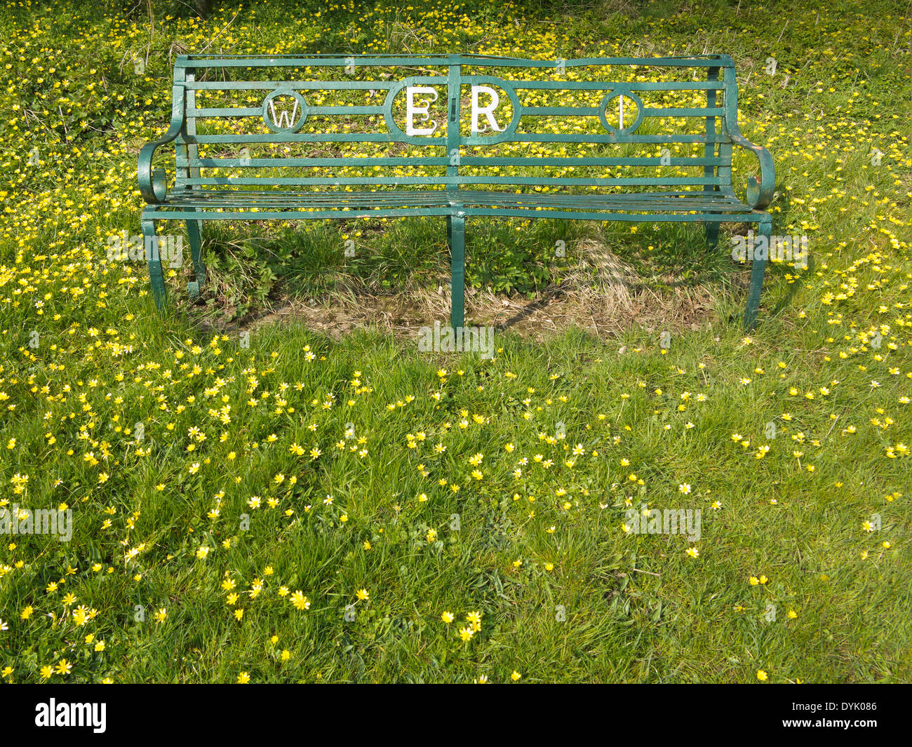 Green wrought iron bench with Women's Institute and Elizabeth Regina reference. On grassy background with lesser celandine Stock Photo