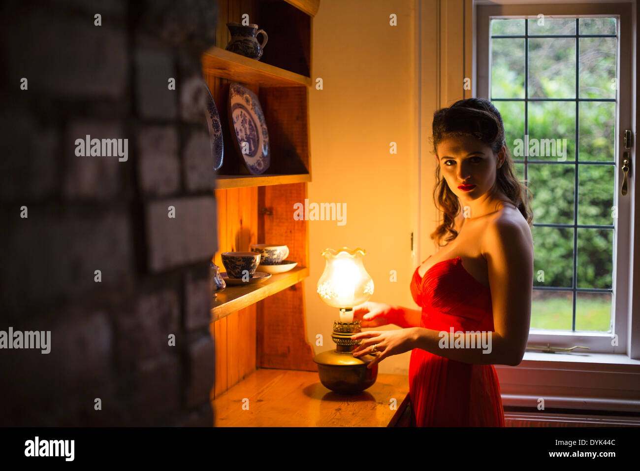 Young woman in an orange, strapless evening dress in front of an old dresser. Stock Photo