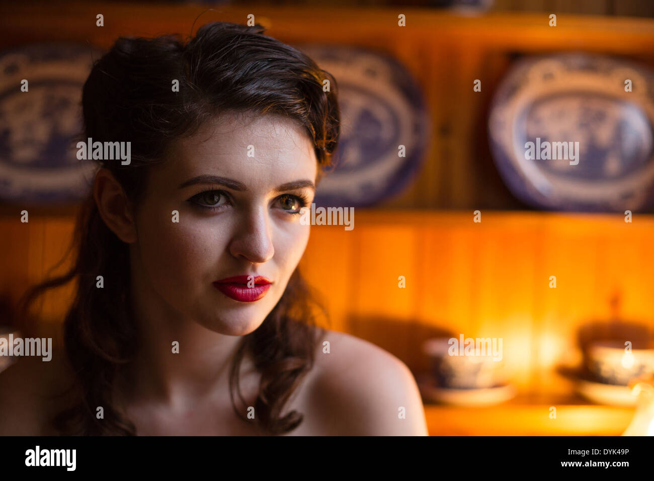 Young woman in an orange, strapless evening dress in front of an old dresser. Stock Photo
