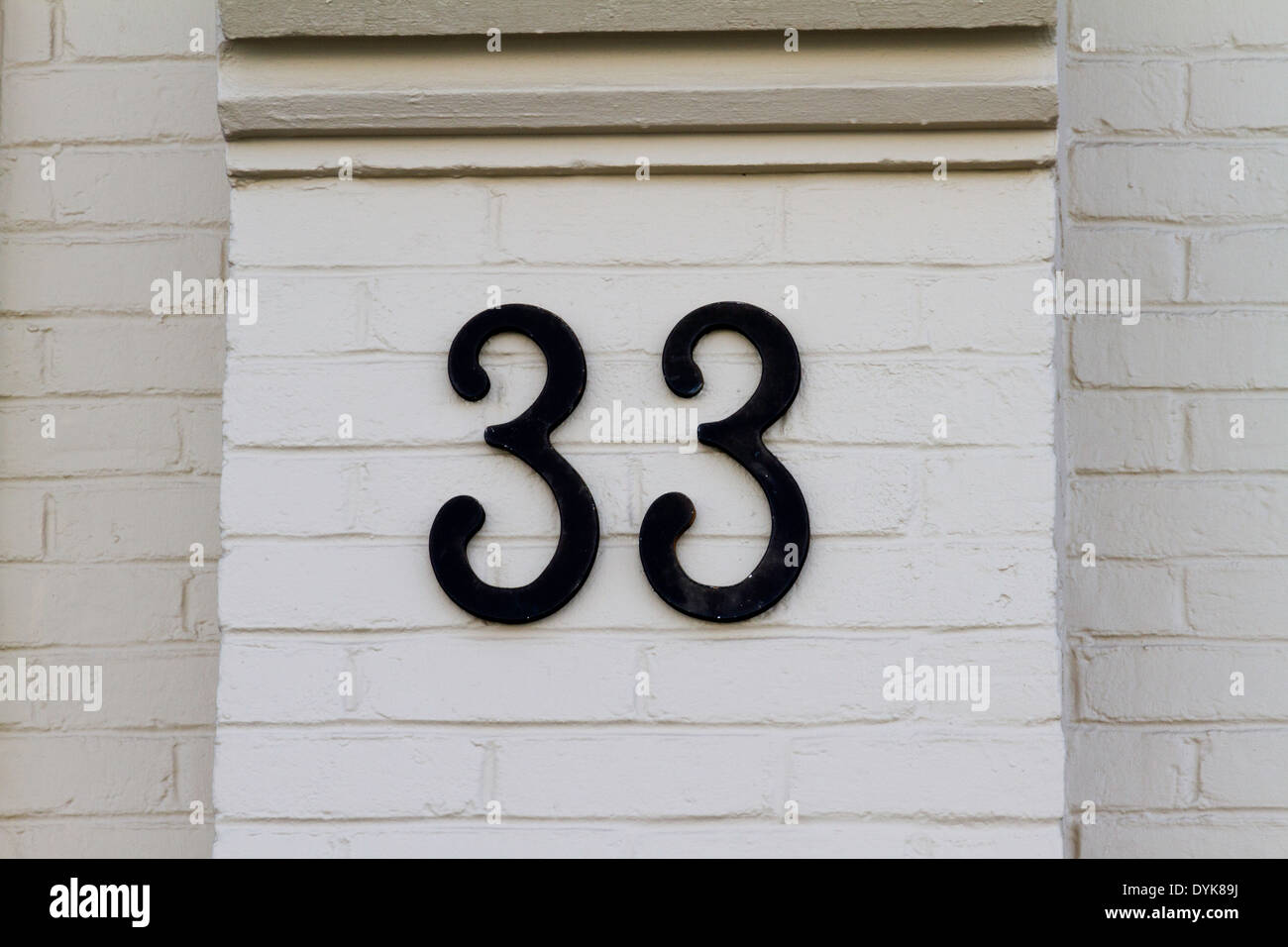 Address number 33 in black wrought iron mounted on a white brick wall
