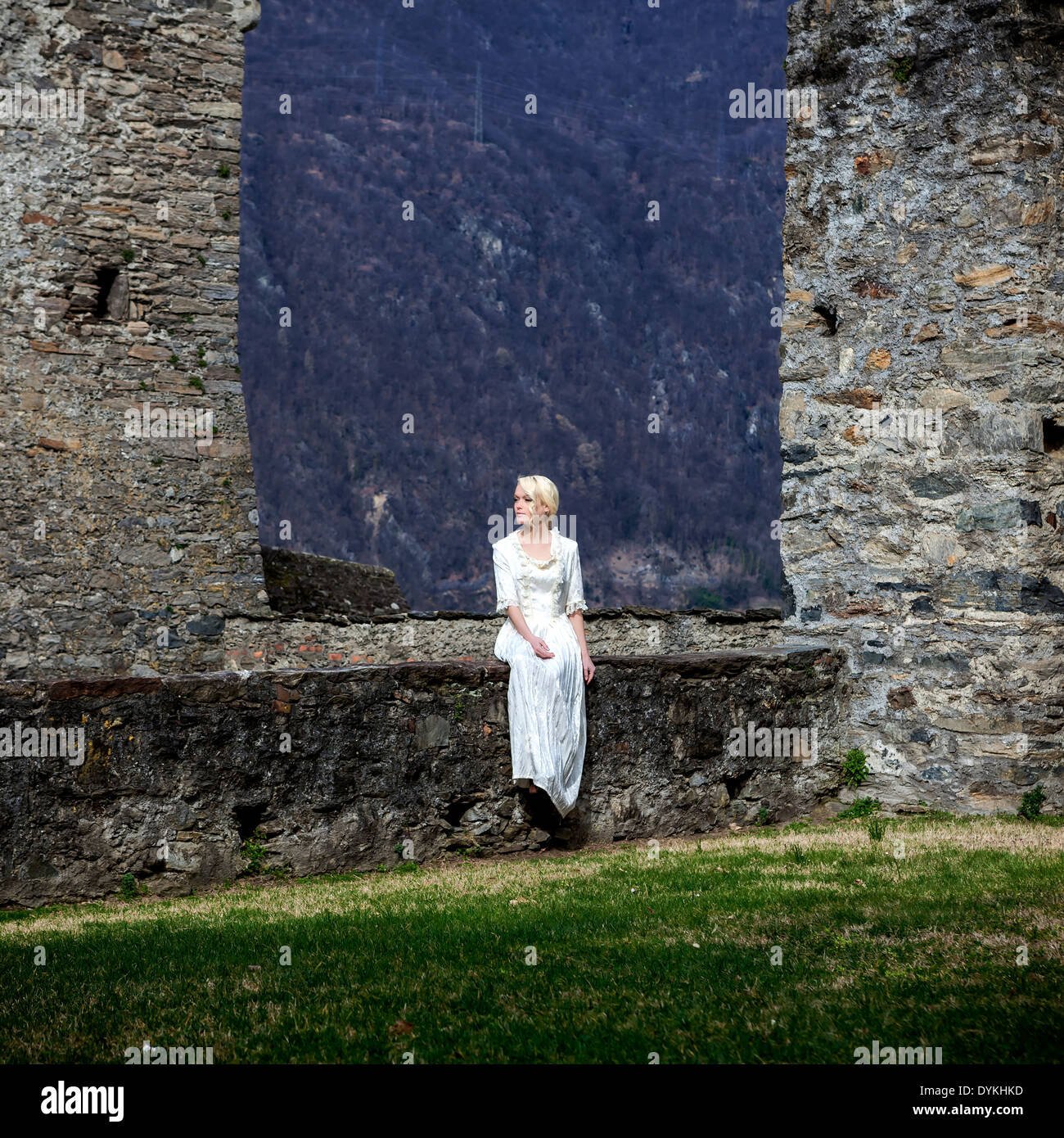 a woman in a white period dress is sitting on a wall at a castle Stock Photo