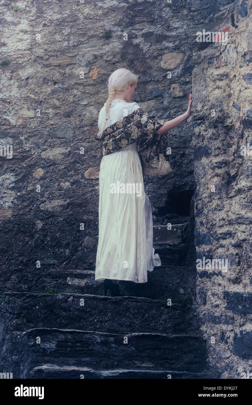 a lady in a white period dress is standing on old stone steps Stock Photo