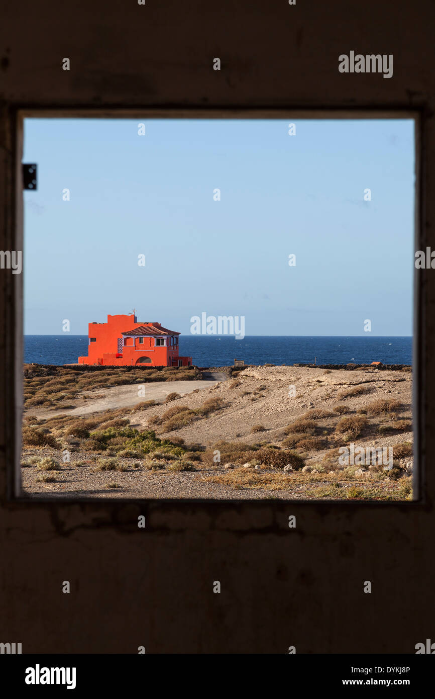 Orange house seen through a window frame with blue sea and sky behind Stock Photo