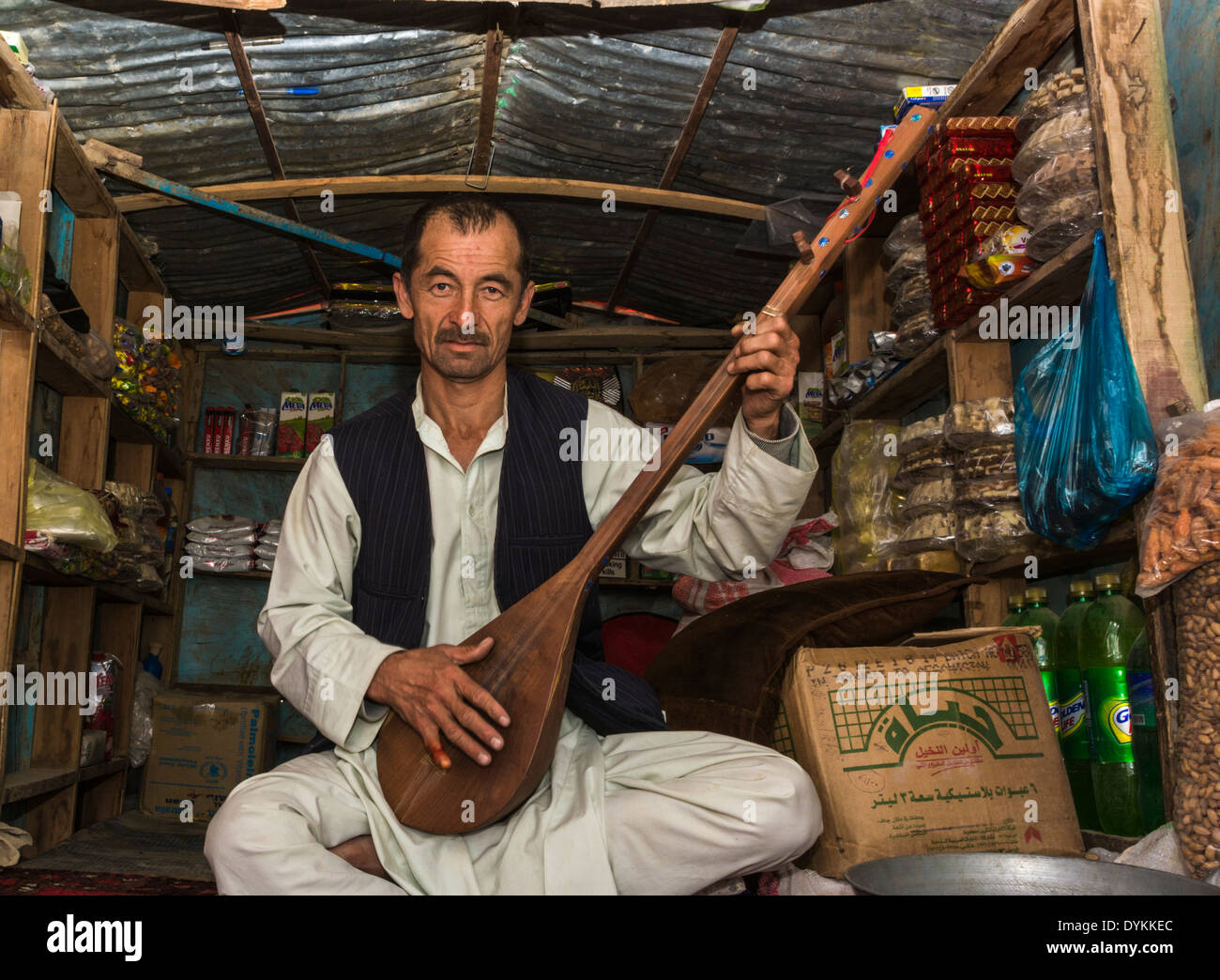 Shopkeeper and musician in Samangan (Afghanistan), sitting in his small shop practicing his traditional string instrument Stock Photo