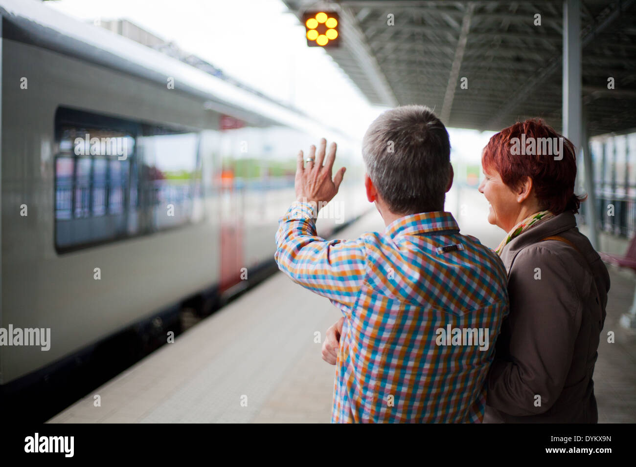 Parents standing on the platform in a railway station waving goodbye as the train with their child leaves the station. Stock Photo