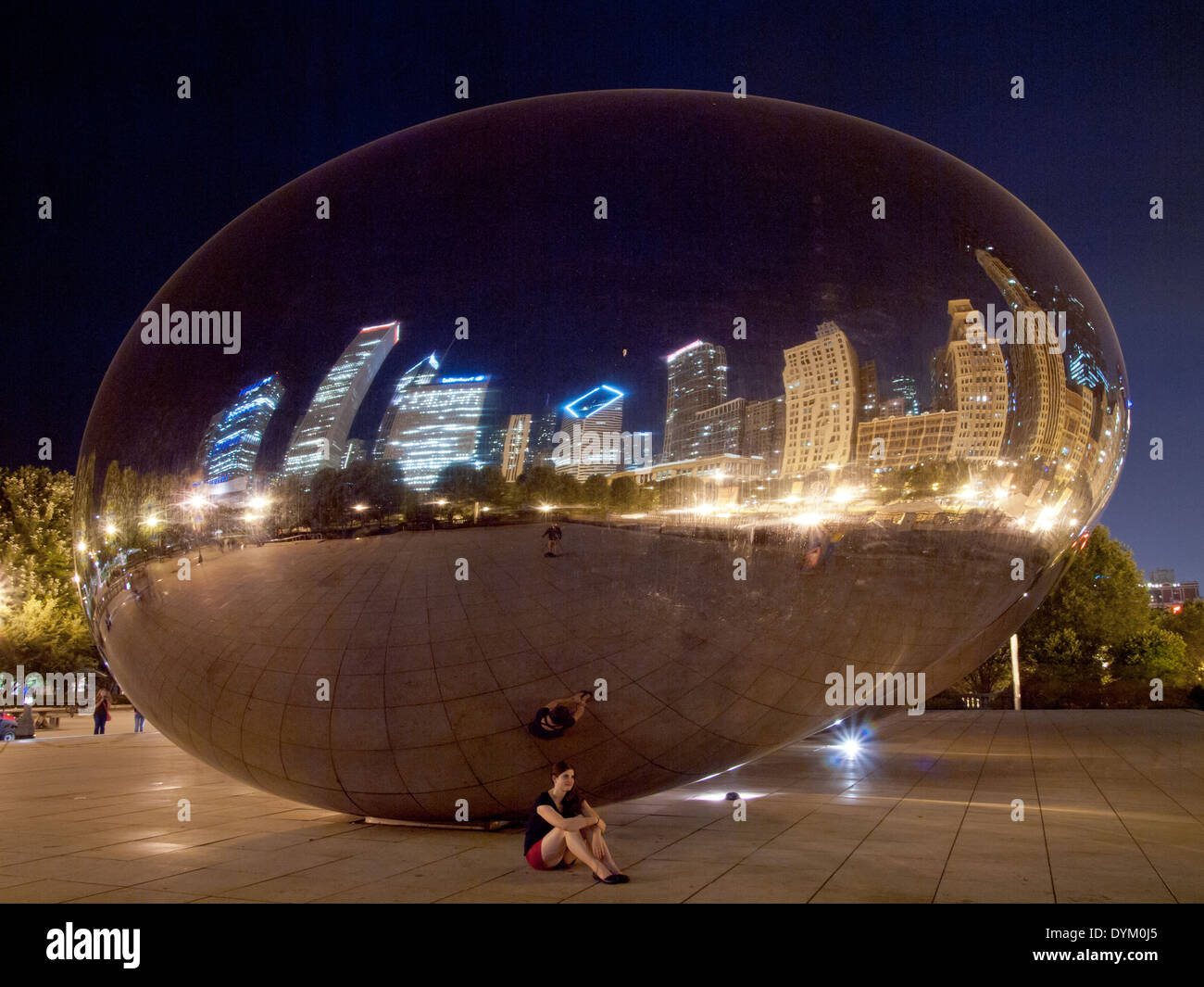 A pretty brunette girl sits beneath Cloud Gate (The Bean) on a summer night in Millennium Park, Chicago, Illinois. Stock Photo