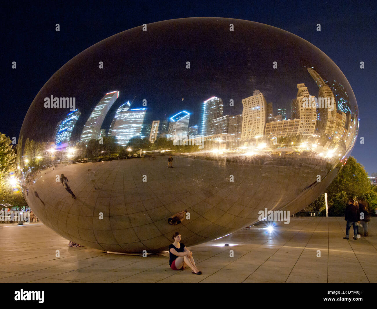 A pretty brunette girl sits beneath Cloud Gate (The Bean) on a summer night in Millennium Park, Chicago, Illinois. Stock Photo