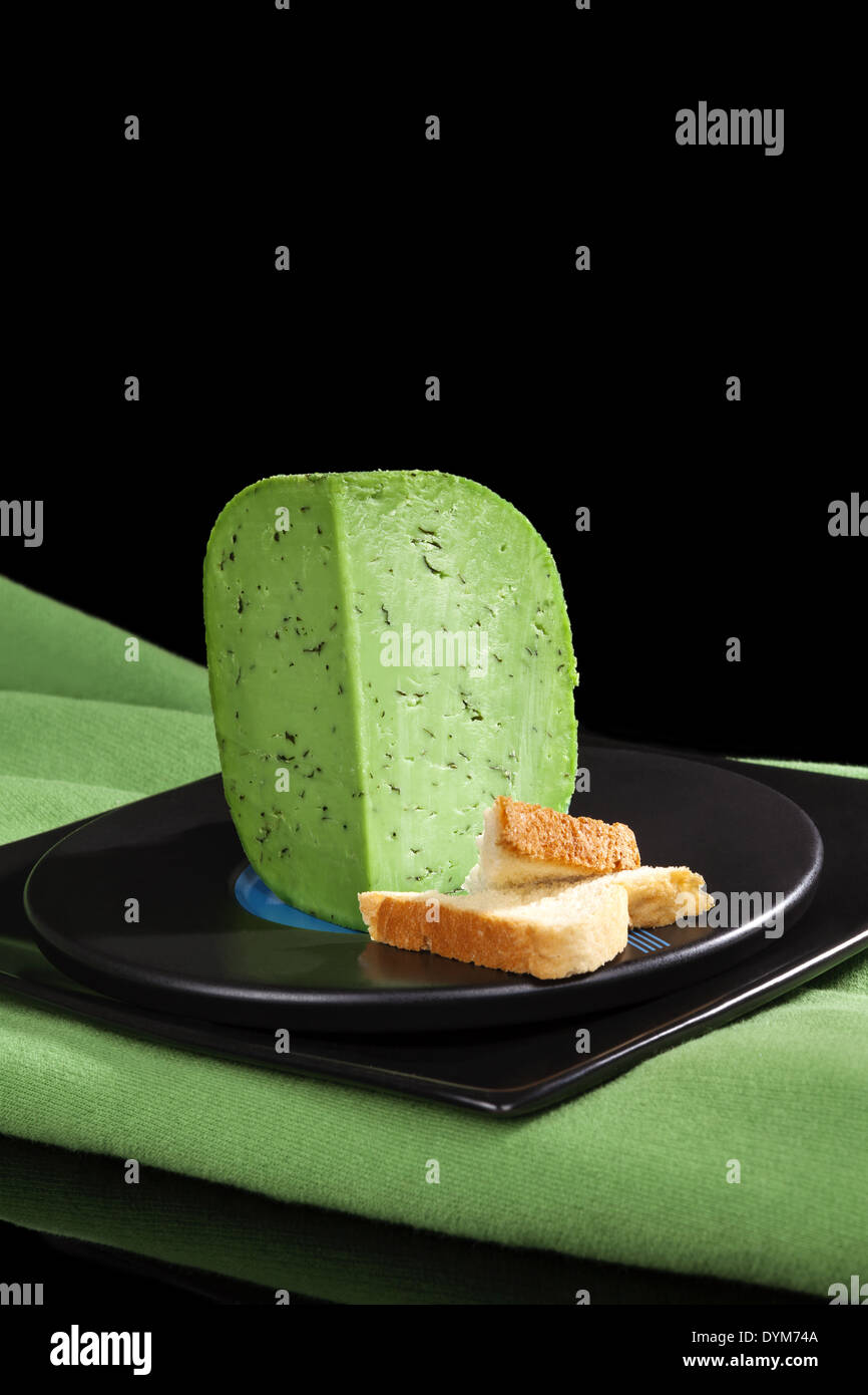 Green pesto gouda cheese piece on black plate on black background