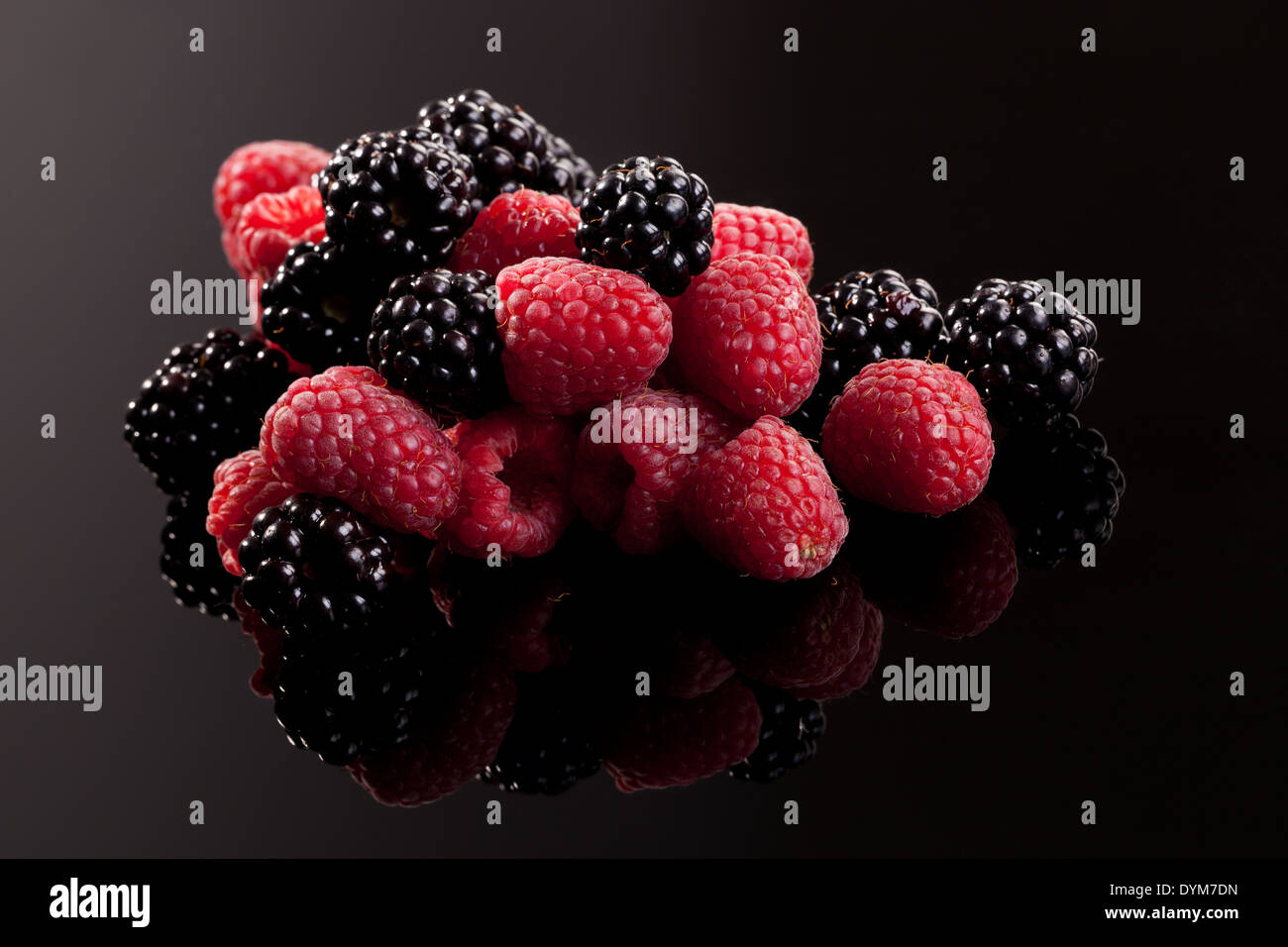 Raspberries and blackberries on black background with reflection
