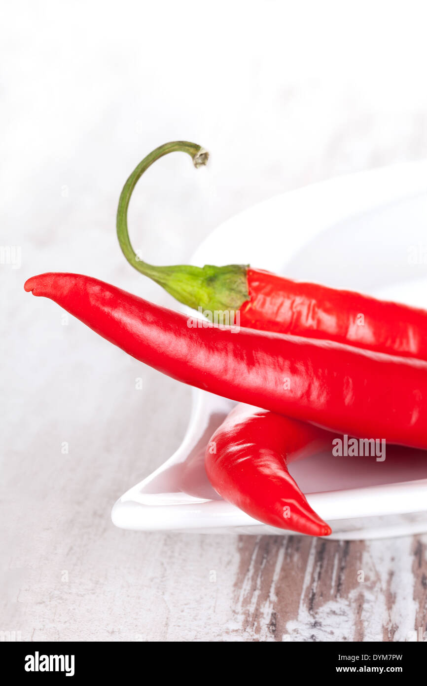 Fresh red hot chili peppers on white tray on white wooden textured background. Culinary cooking ingredients. Stock Photo