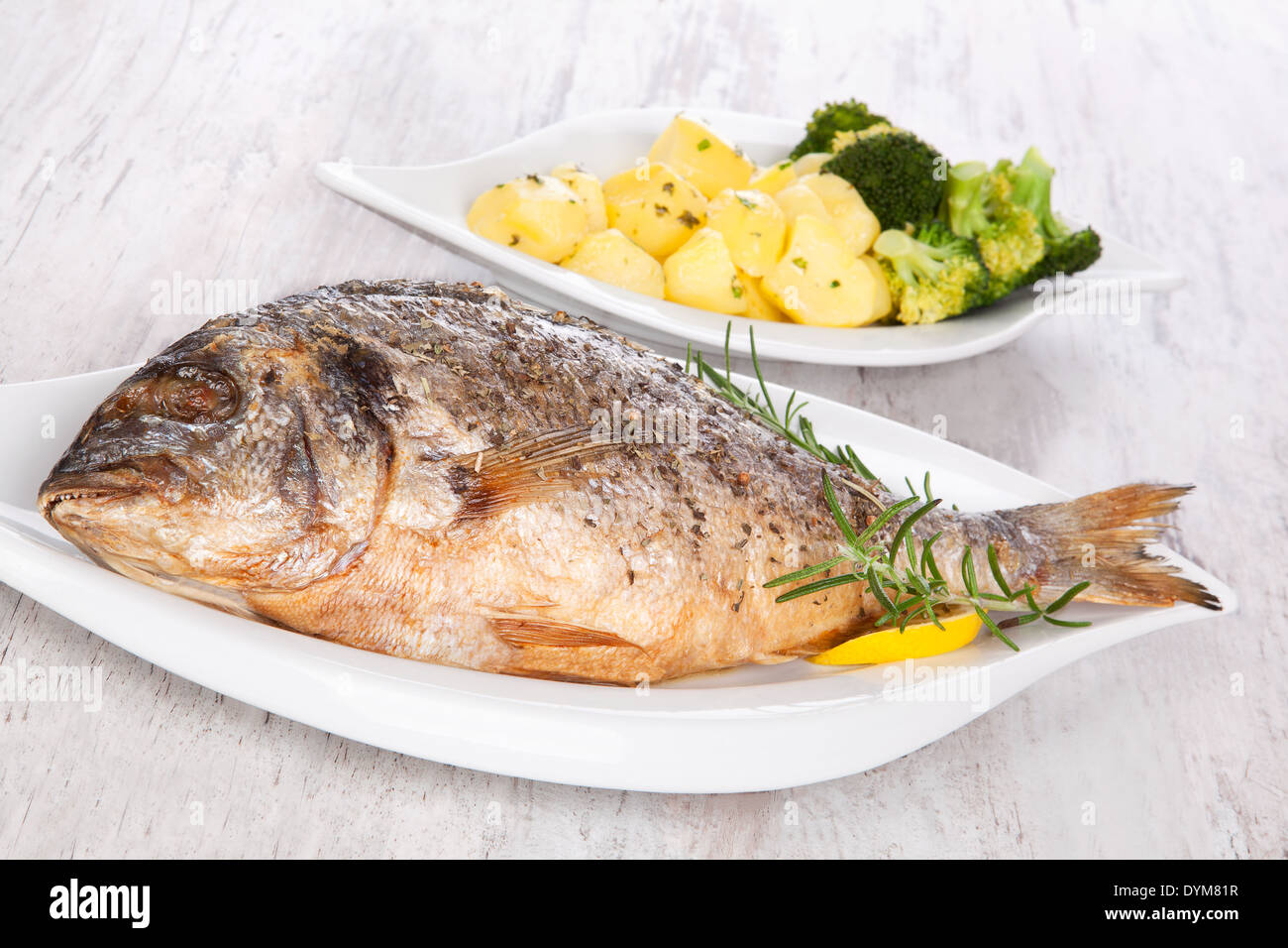 Grilled gilt head sea bream on plate with lemon and rosemary and potatoes. Mediterranean bright seafood background. Stock Photo