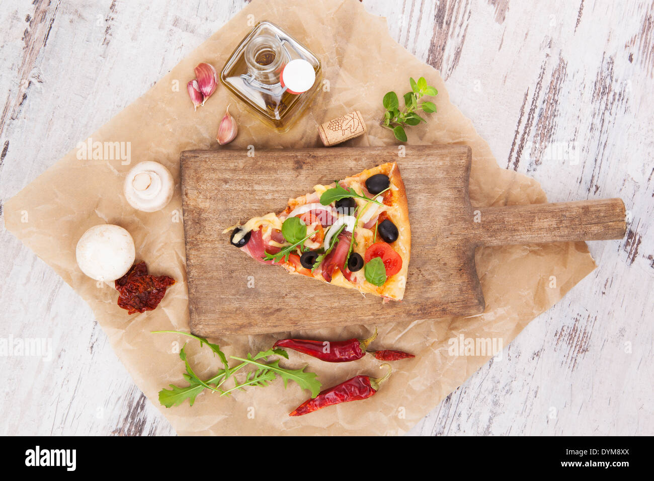 Culinary pizza cooking. Pizza piece on wooden kitchen board, with various ingredients and toppings. Fresh herbs, olive oil Stock Photo