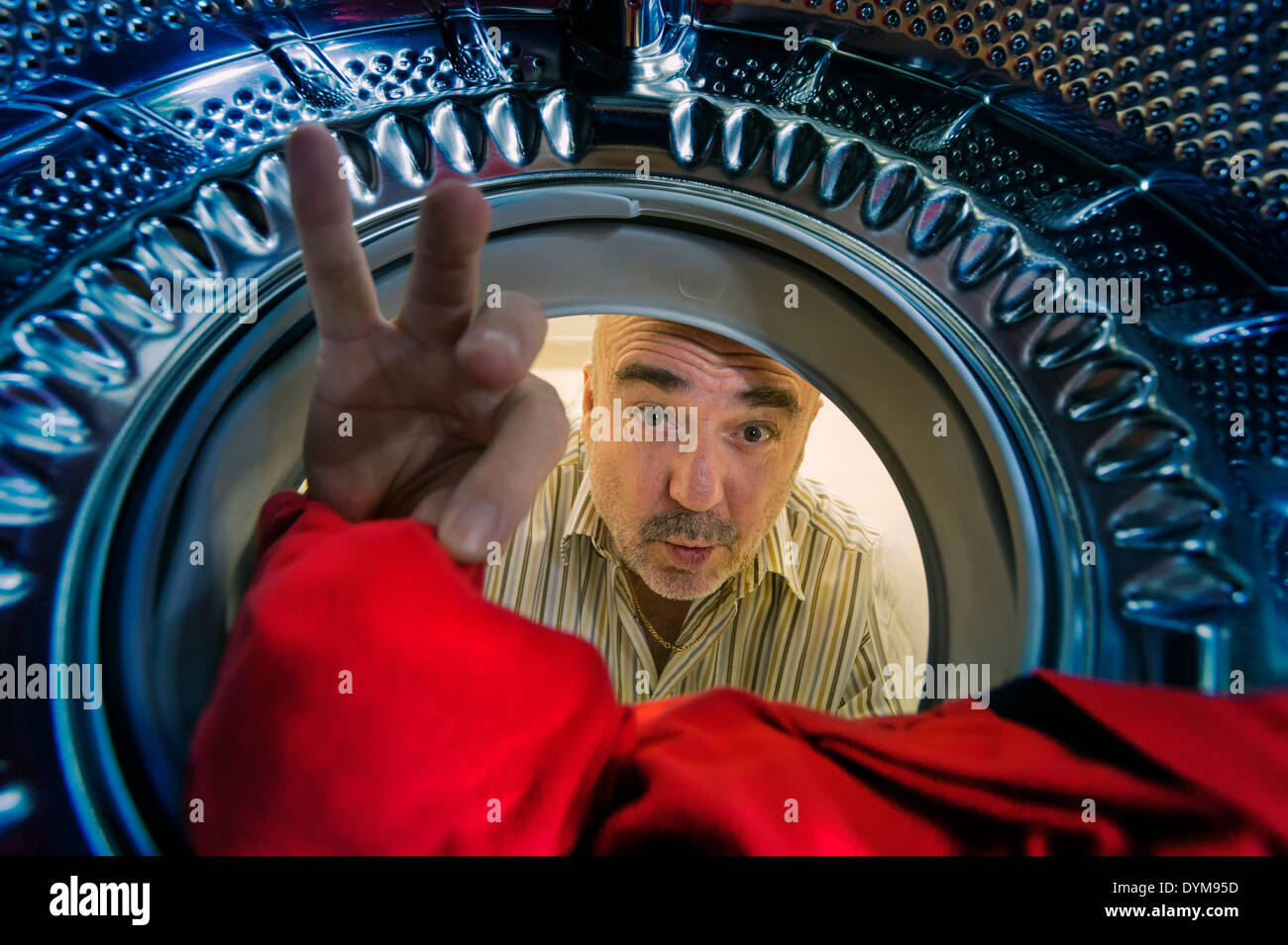 Man looking into a washing machine, grabbing a red cloth, Germany Stock Photo
