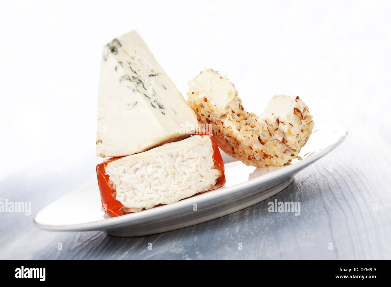 Goat cheese, blue cheese and cream cheese on white plate on blue wooden background. Culinary cheese eating. Stock Photo