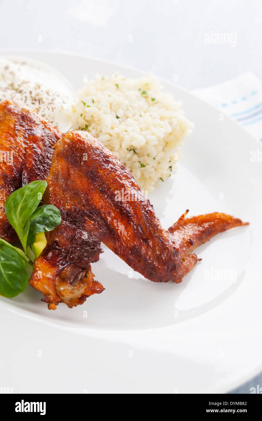 Barbeque chicken wing with rice, salad and dressing on white plate on