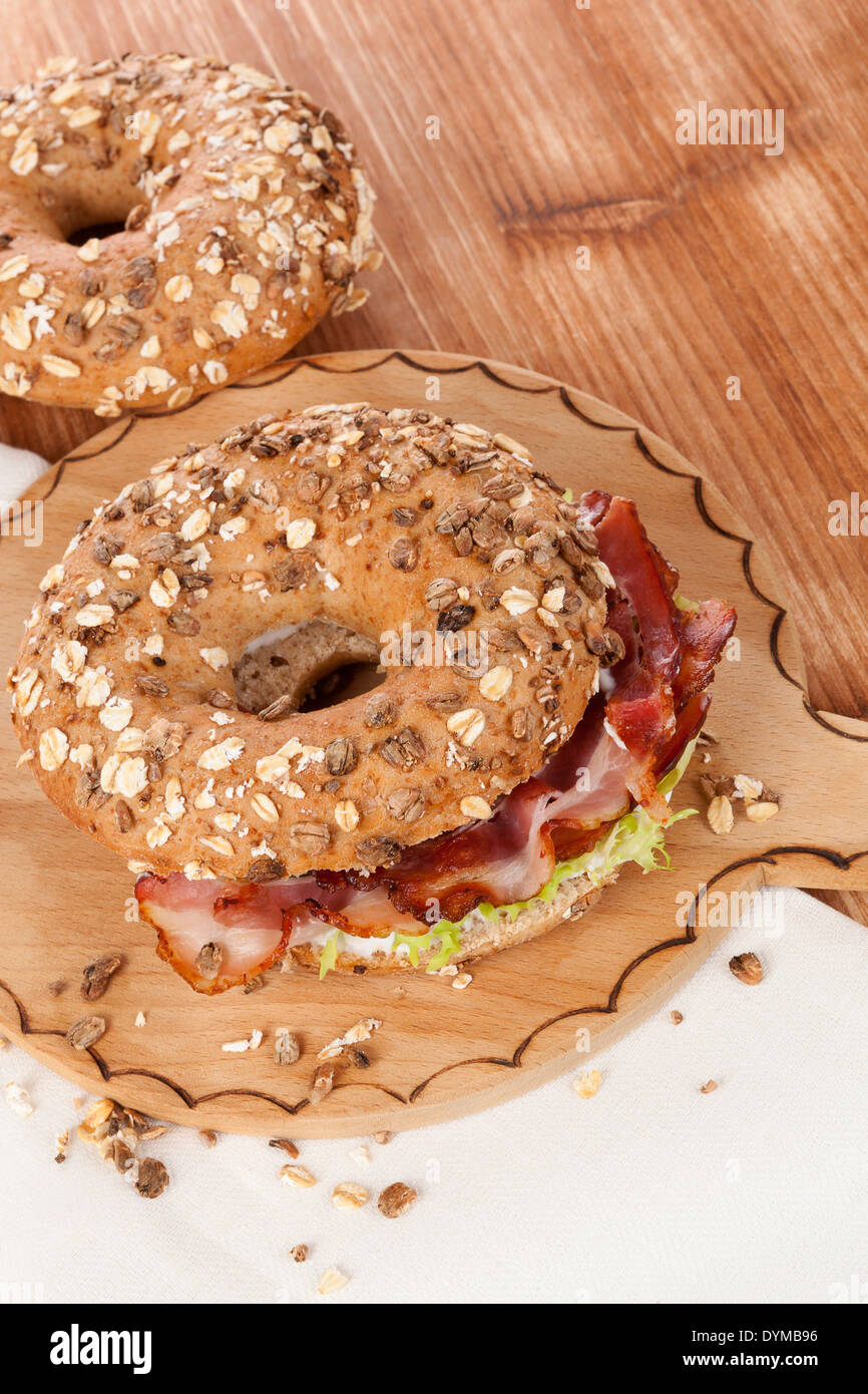 Delicious bagel eating. Whole grain bagel with bacon on wooden background. Stock Photo