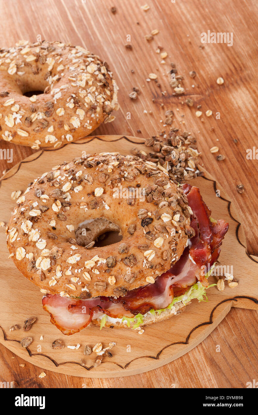 Whole grain bagel with bacon on wooden background. Culinary bagel eating. Stock Photo