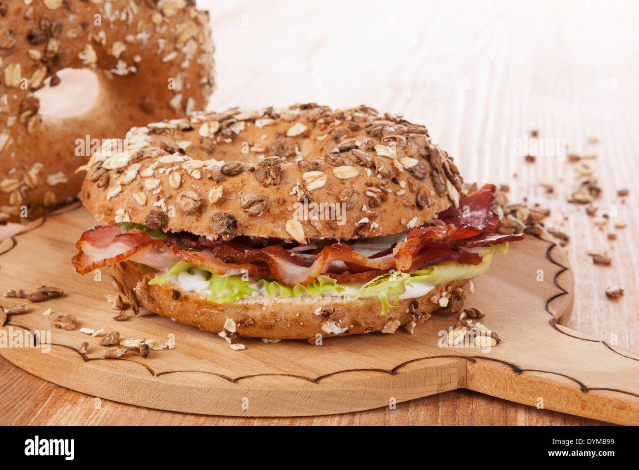 Whole grain bagel with bacon on wooden kitchen board on wooden background. Traditional bagel eating. Stock Photo