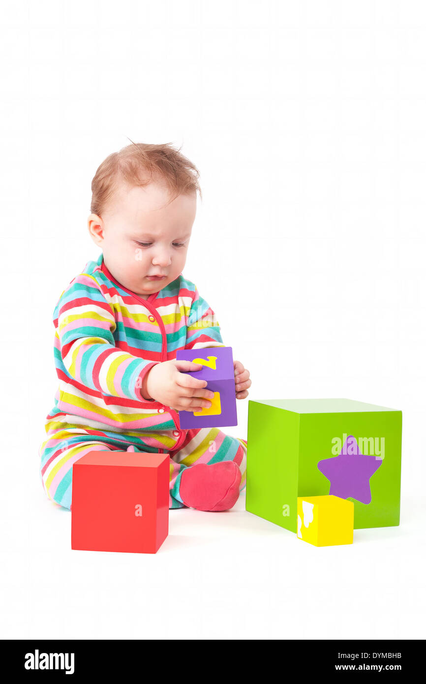 Cute one year old baby girl in colorful clothing playing with colorful blocks isolated on white background. Creativity Stock Photo