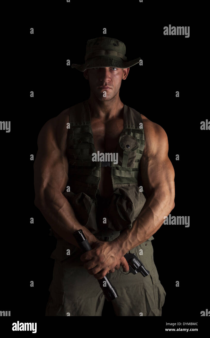 Serious young muscular soldier with gun and flashlight in green uniform standing proud isolated on black background. Army Stock Photo
