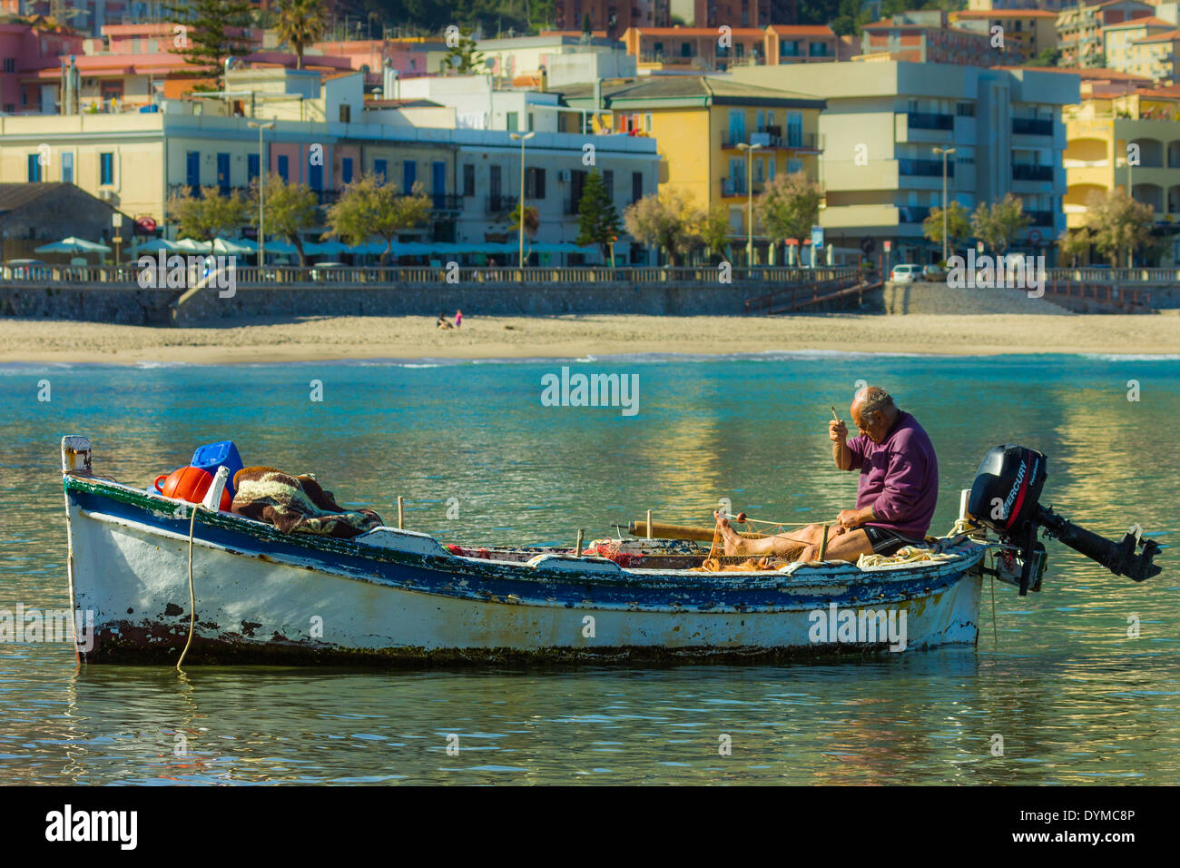 Fisherman mending a net in his boat at this popular historic tourist town; Cefalu, Palermo Province, Sicily, Italy Stock Photo