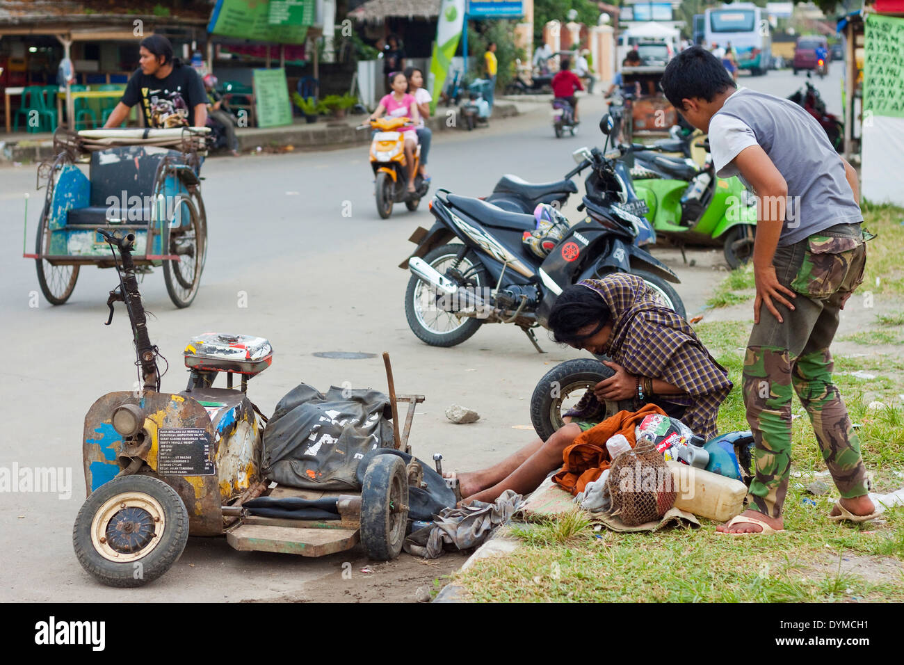Young scooter enthusiasts mending a puncture on the seafront of this