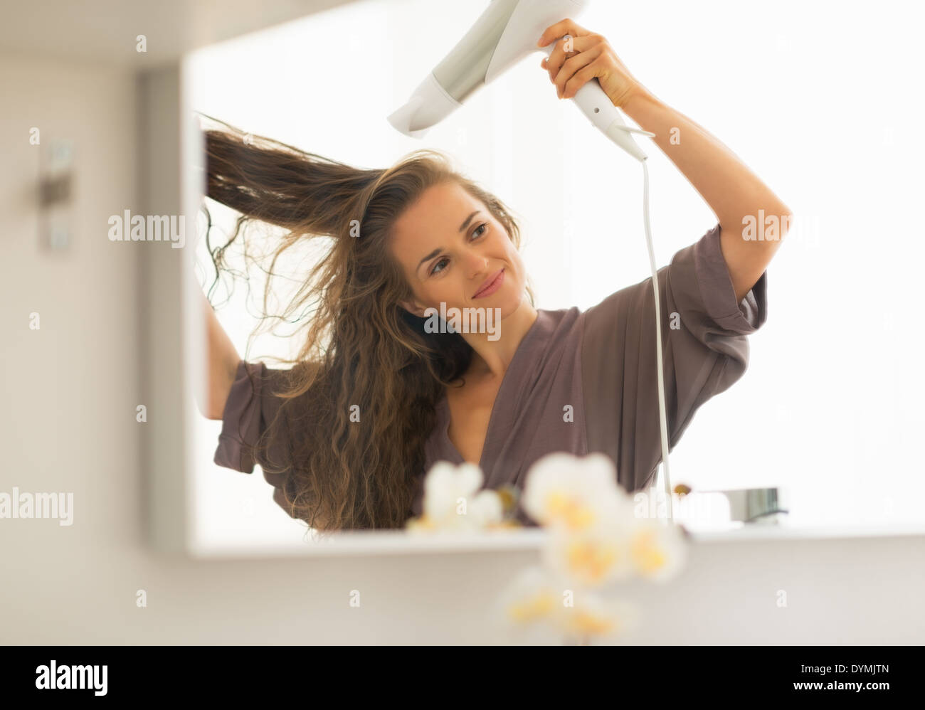 Young woman blow drying hair in bathroom Stock Photo - Alamy