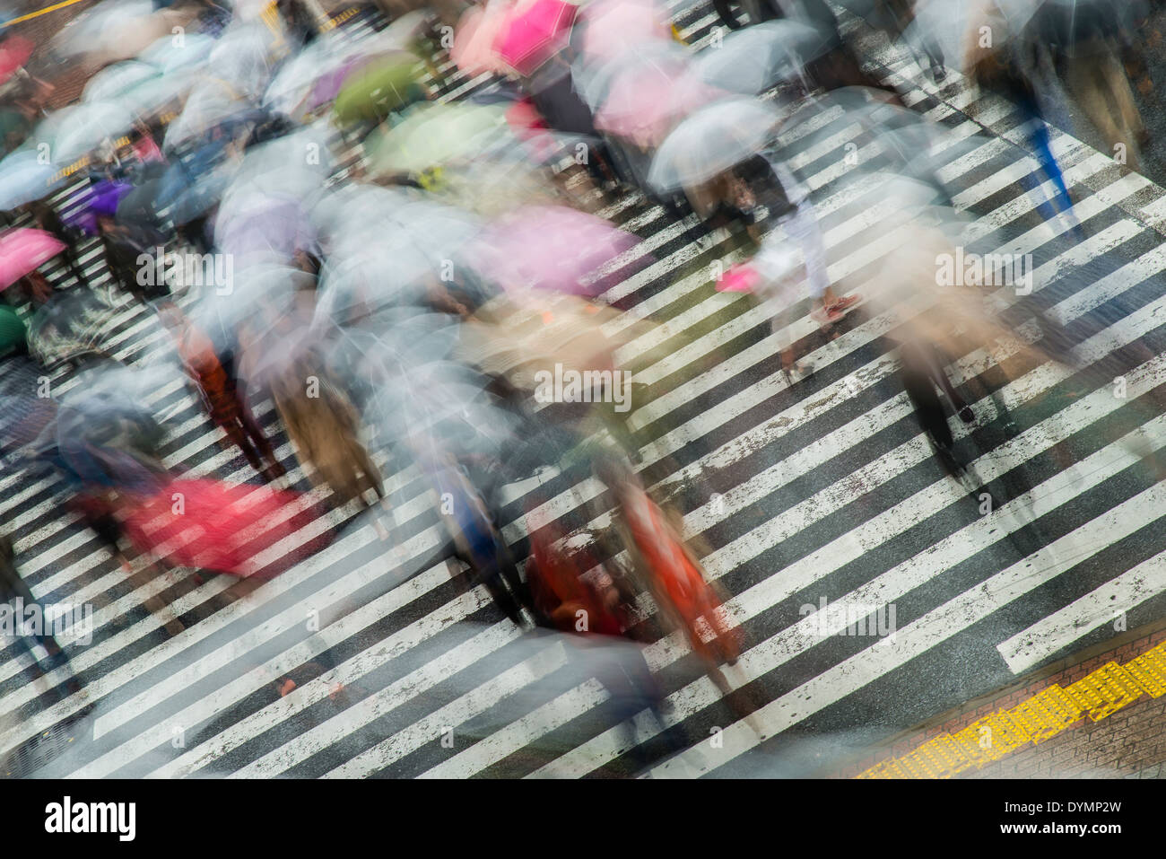 Blurred pedestrians with umbrellas crossing the street at Shibuya crossing, Tokyo, Japan Stock Photo
