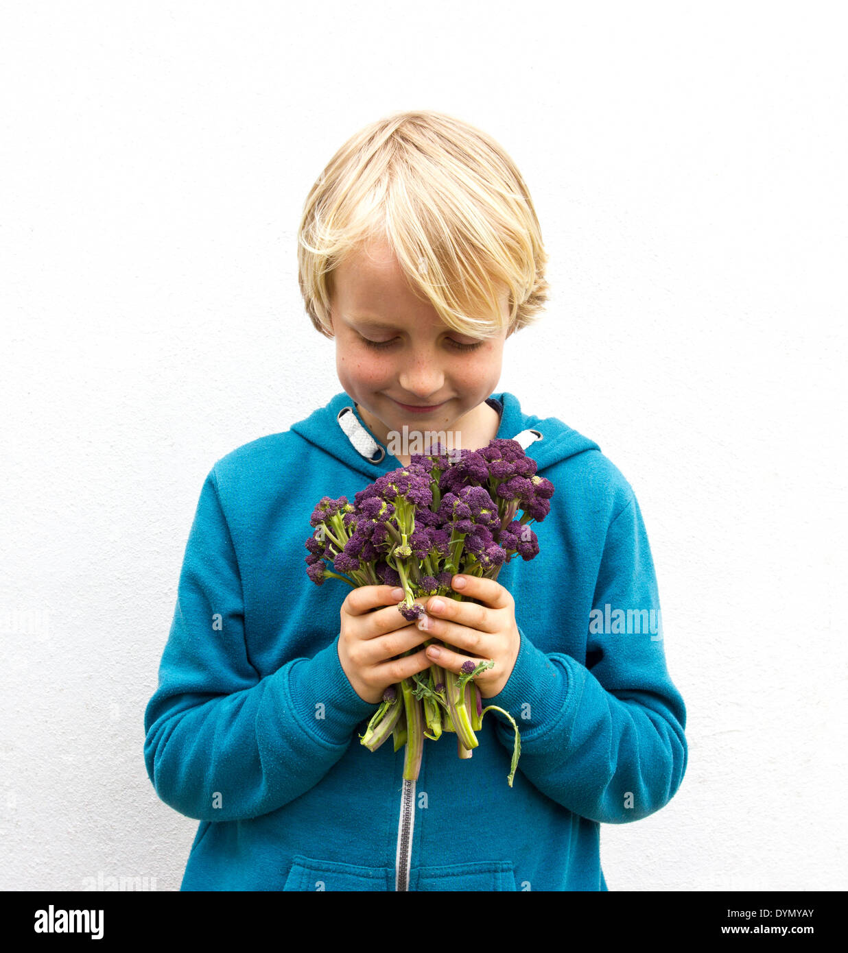 Blond boy with freckles wearing a blue top holding a bunch of purple sprouting broccoli Stock Photo