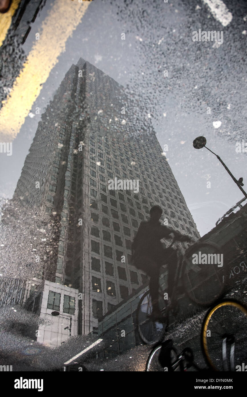 reflection in wet pavement of canary wharf and cyclist Stock Photo