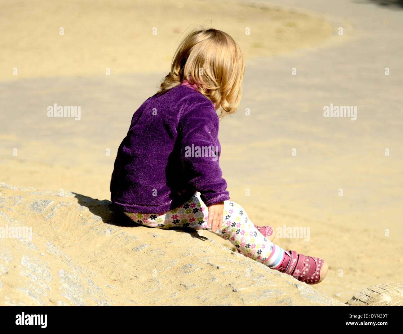 Lonely child sitting on a hill at a playground Stock Photo