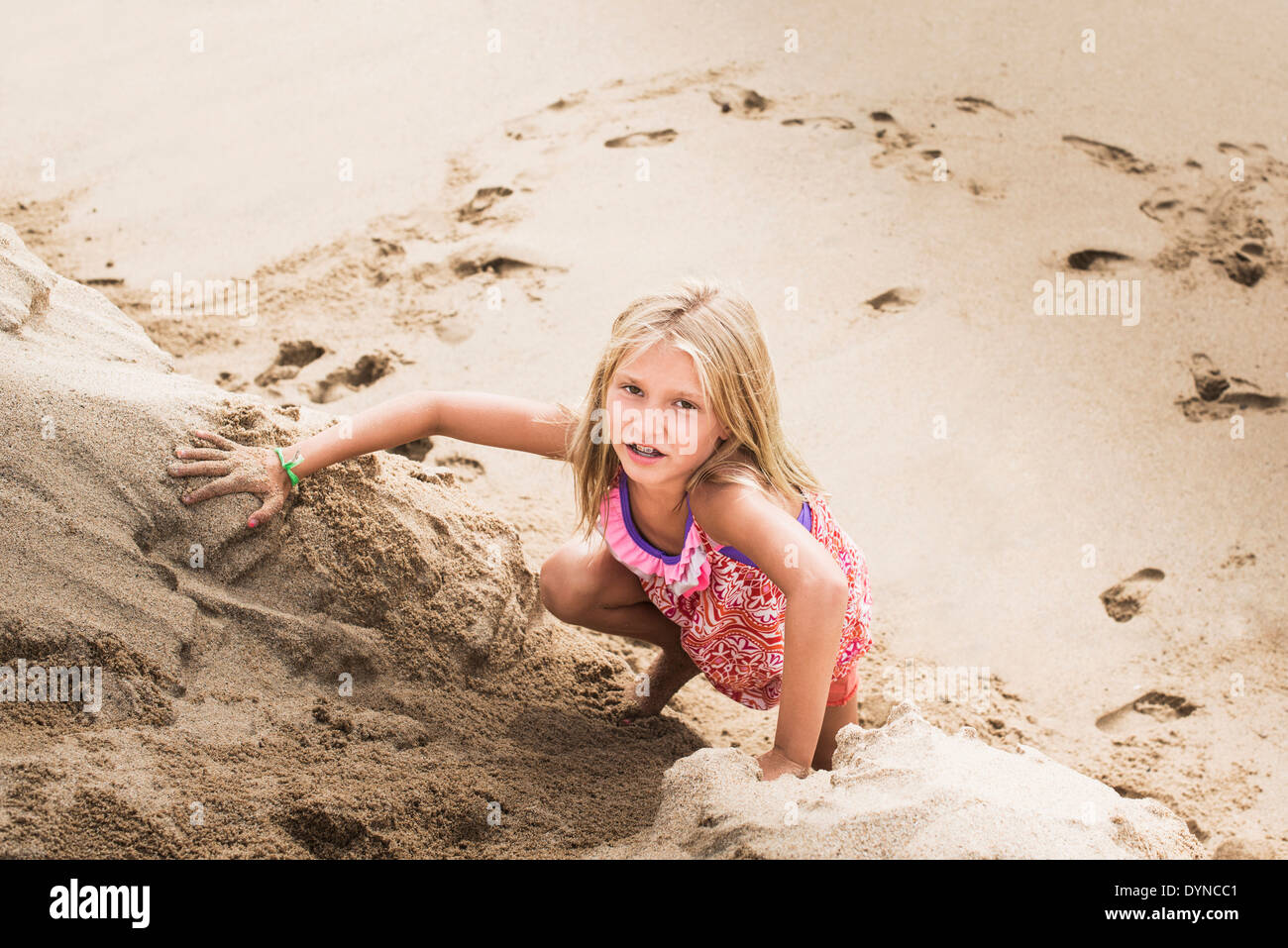 Caucasian girl climbing sand hill on beach Stock Photo