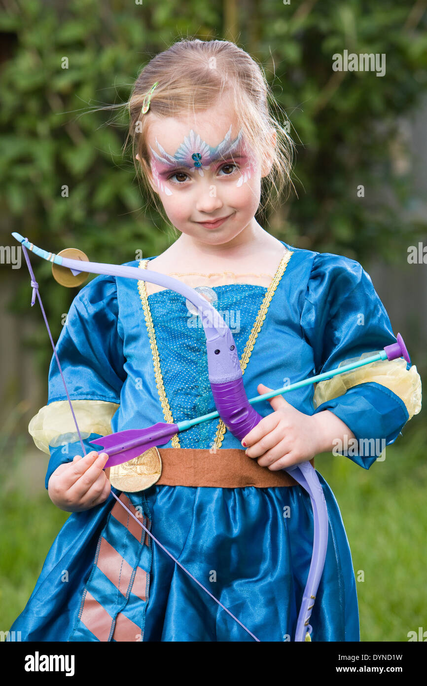 A young girl standing outside wearing a fancy dress princess outfit and wearing face paint Stock Photo