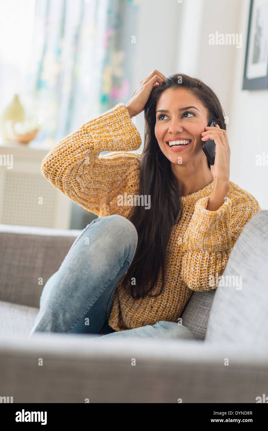 Hispanic woman talking on cell phone on sofa Stock Photo