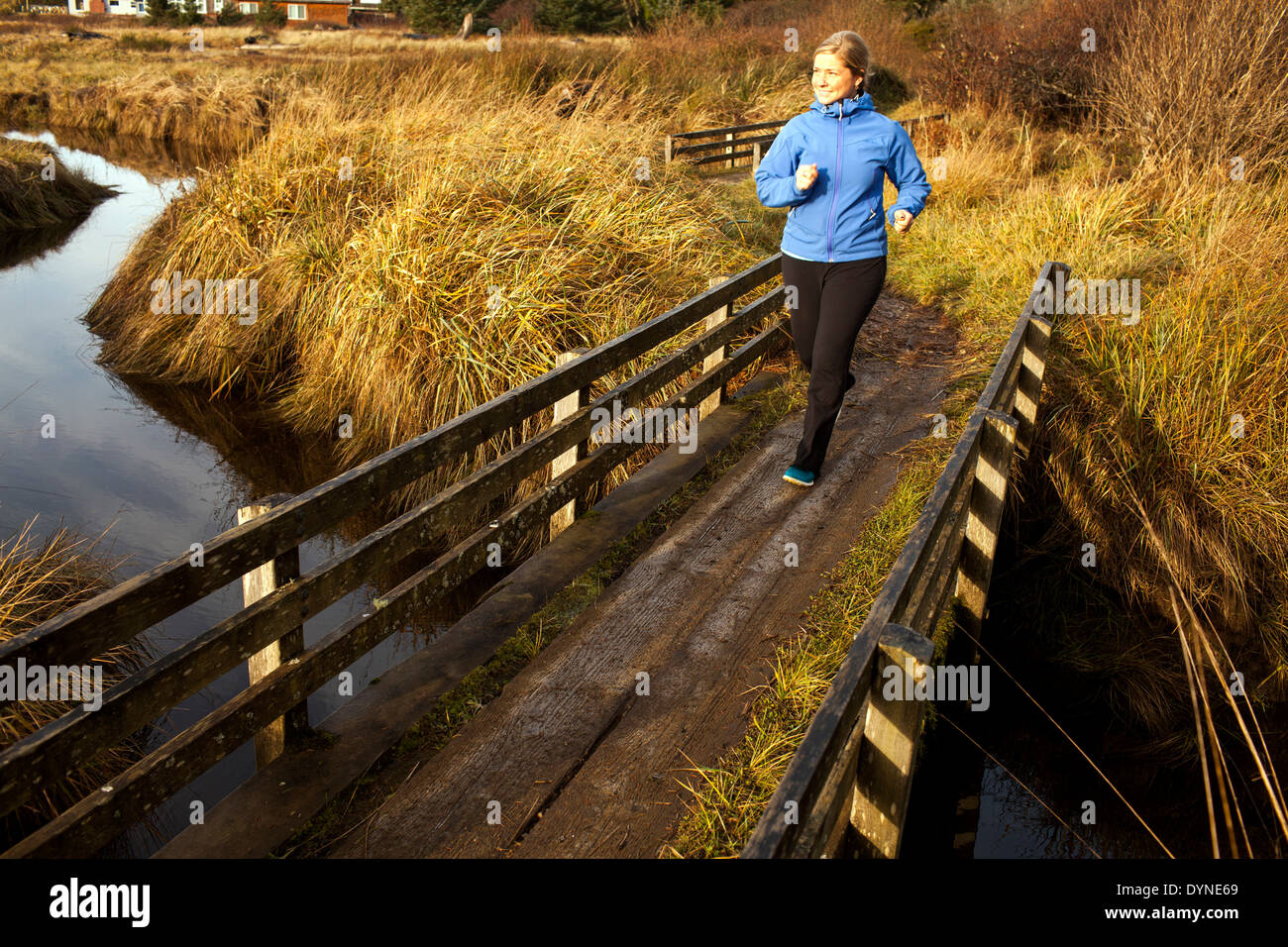 Caucasian woman jogging on wood bridge over creek Stock Photo
