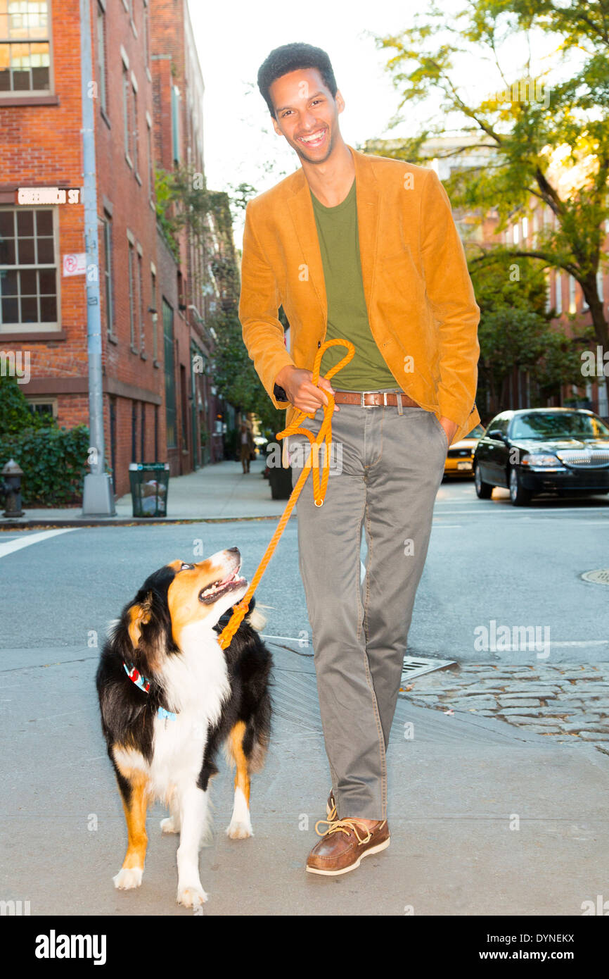 Mixed race man walking dog on city street Stock Photo
