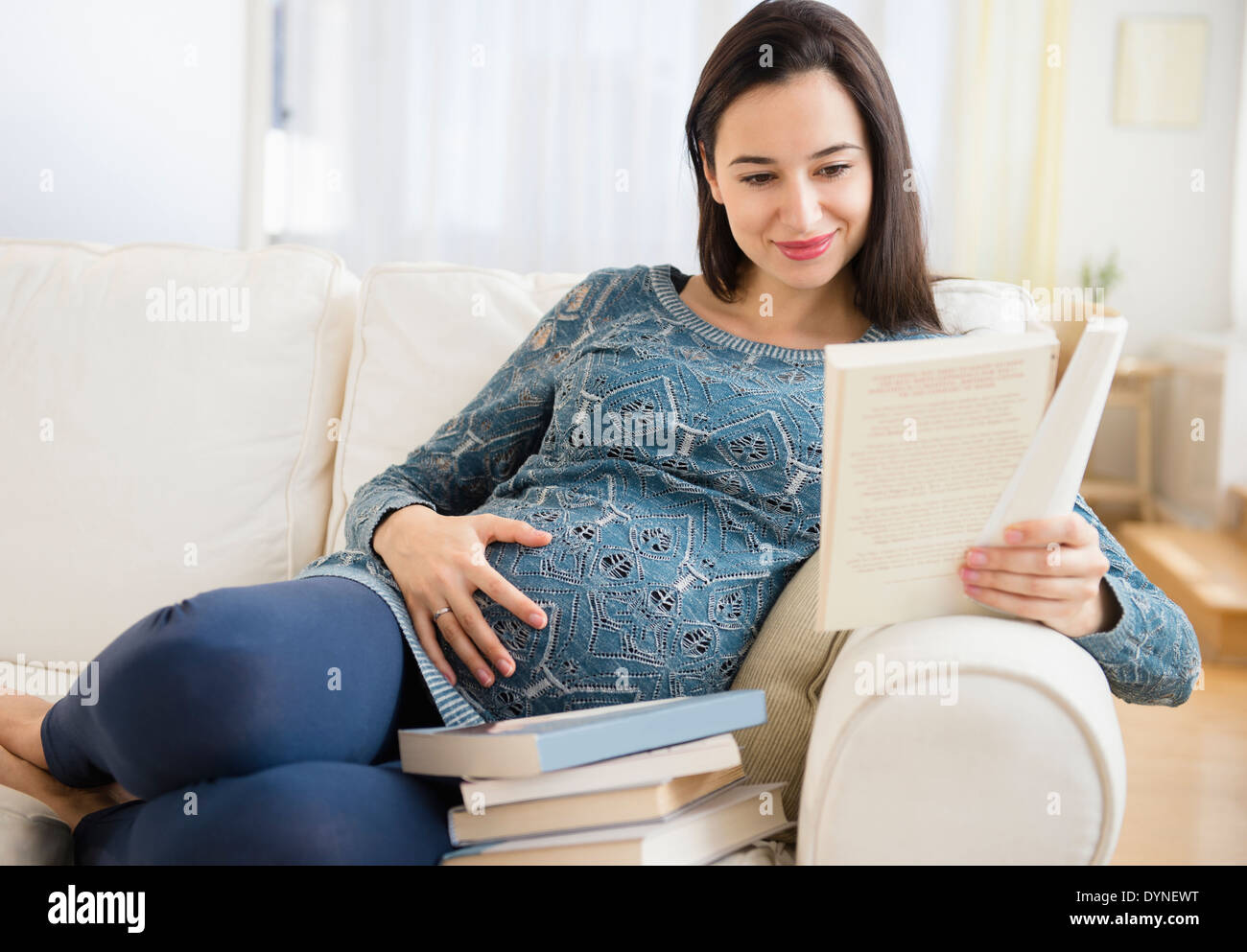 Pregnant Caucasian woman reading baby books on sofa Stock Photo