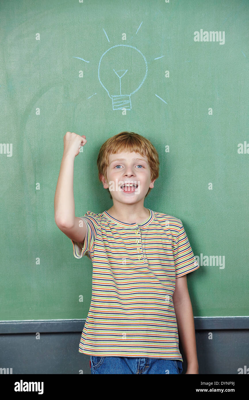 Cheering boy has idea with lightbulb drawn on chalkboard Stock Photo