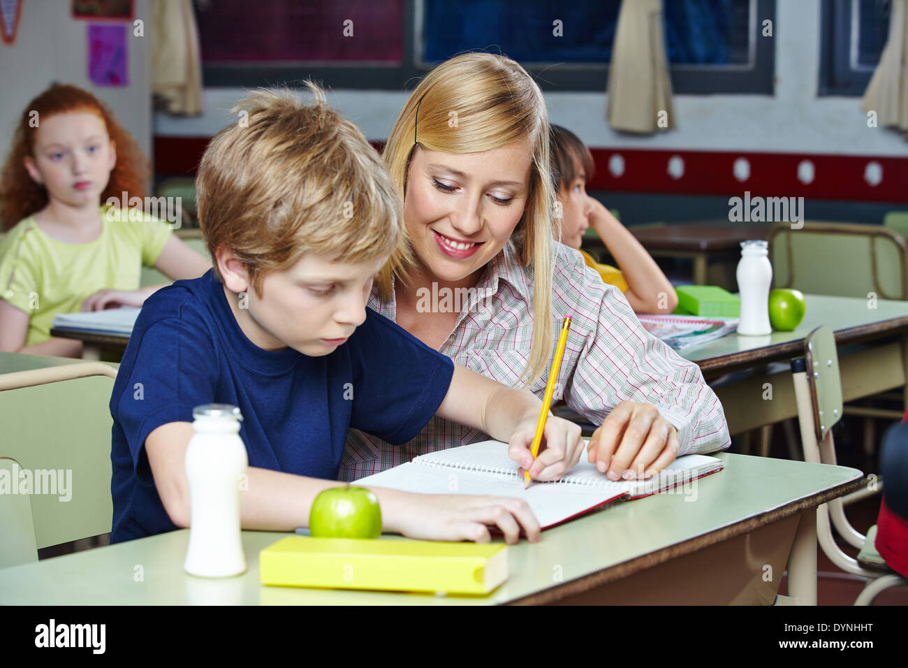 Elementary school teacher helping student in classroom at his desk Stock Photo