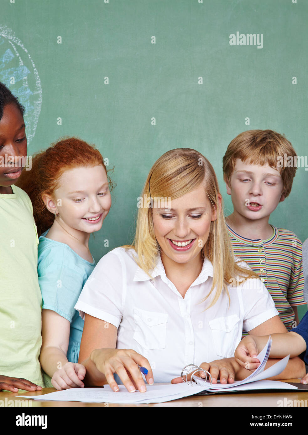 Elementary school students looking at teacher working in class at her desk Stock Photo