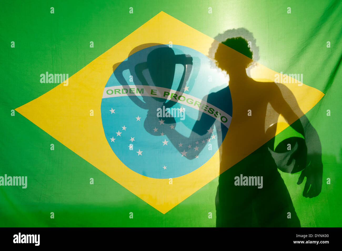 Shadow of Brazilian holding trophy and football in the sun against Brazil flag Stock Photo