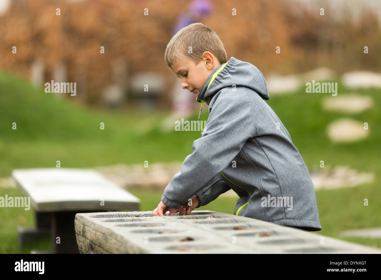 Young caucasian boy playing mancala outdoors during spring. Trademarks on jacket have been removed. Stock Photo