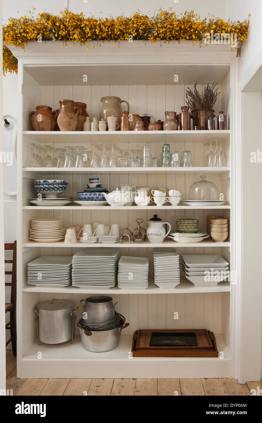 A variety of glassware, earthenware and crockery stored in an open white wooden shelf Stock Photo