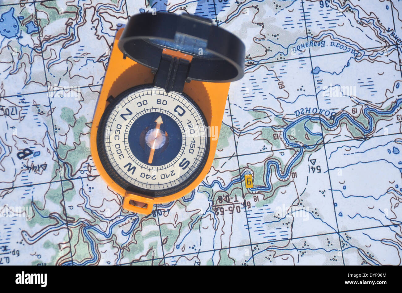 Compass in the black case on an orange ground open the mirror cover is located on a topographic map. Stock Photo