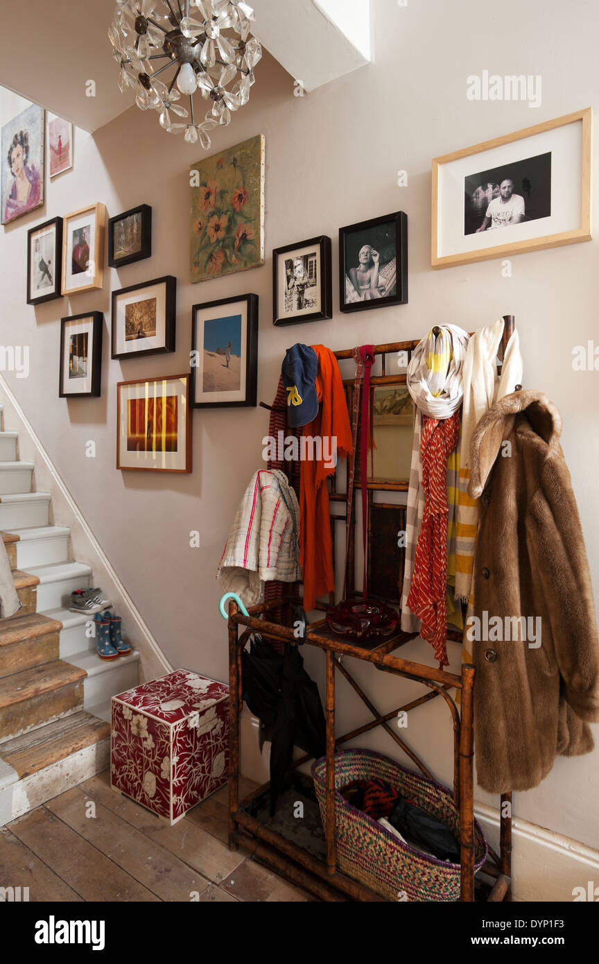 Fur coat and assorted scarves on bamboo coat rack in entrance hall. Framed family photographs adorn the wall Stock Photo