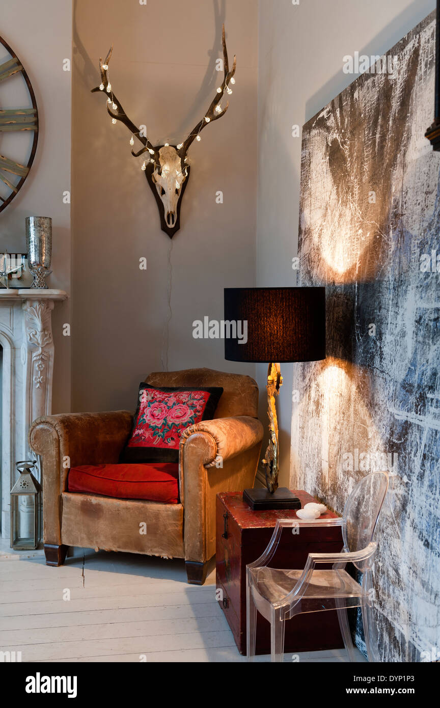 Fairy lights adorn a mounted stag head with antlers on wall above vintage leather armchair Stock Photo
