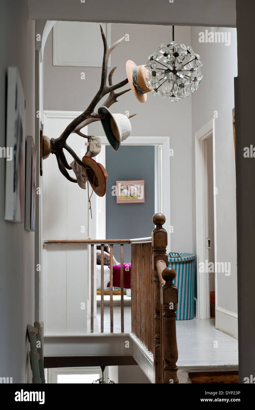 Mounted antlers double up as a hat rack on the wall of a landing with wooden balustrade Stock Photo