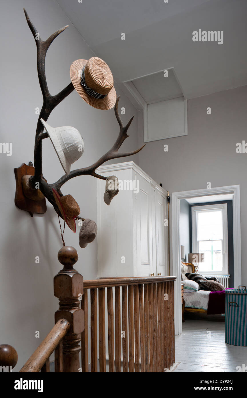 Mounted antlers double up as a hat rack on the wall of a landing with wooden balustrade Stock Photo
