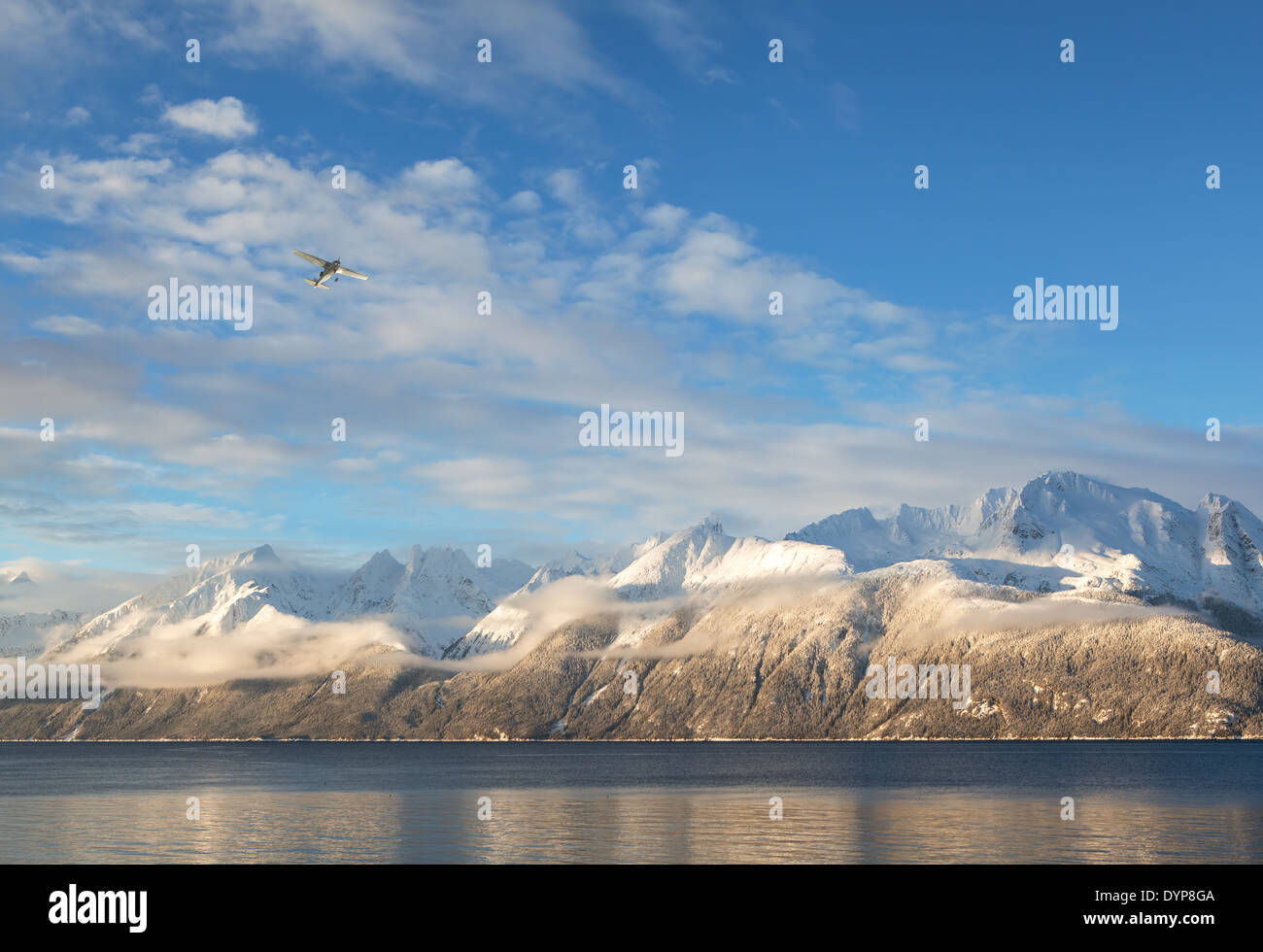 Small airplane flying over the Lynn Canal near Haines Alaska in evening light with snow covered mountains in the background. Stock Photo